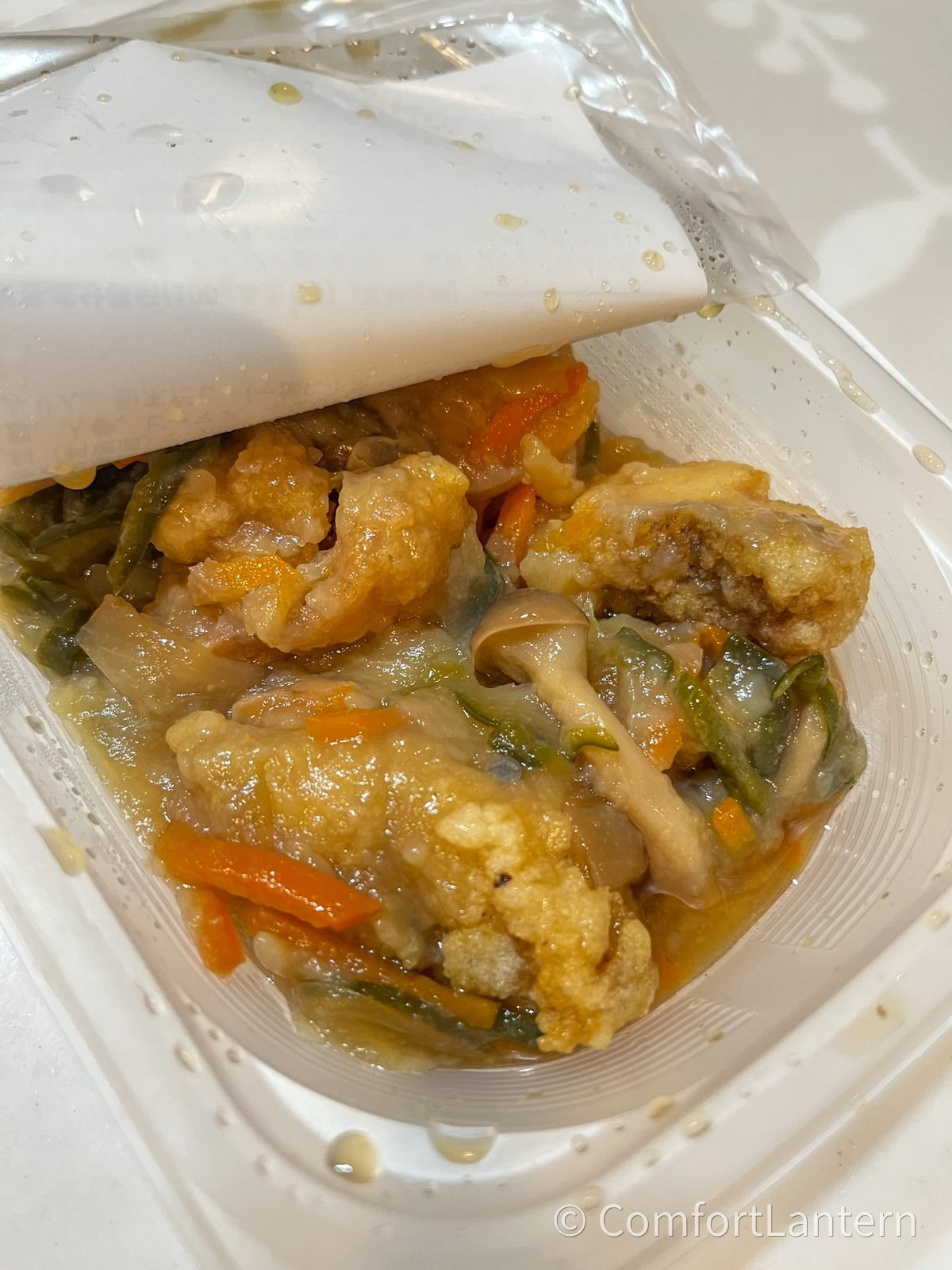 ふわ揚げ白身魚の野菜あんかけの蓋を取ったところ。衣をまとった白身魚に、にんじんと万願寺とうがらしの入ったあんがかかっている