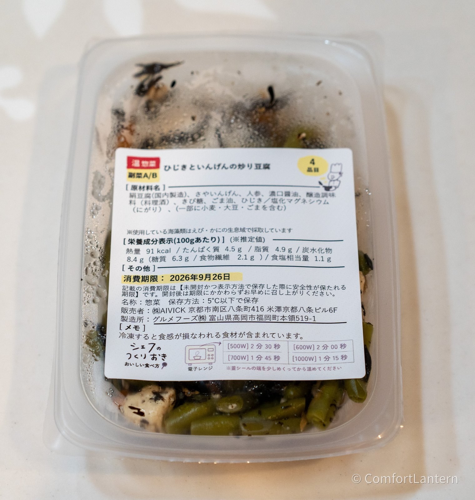 ひじきといんげんの炒り豆腐の容器に貼られたラベル。原材料に絹豆腐(国内製造)、さやいんげん、人参、ごま油、ひじきなどが並んでいる
